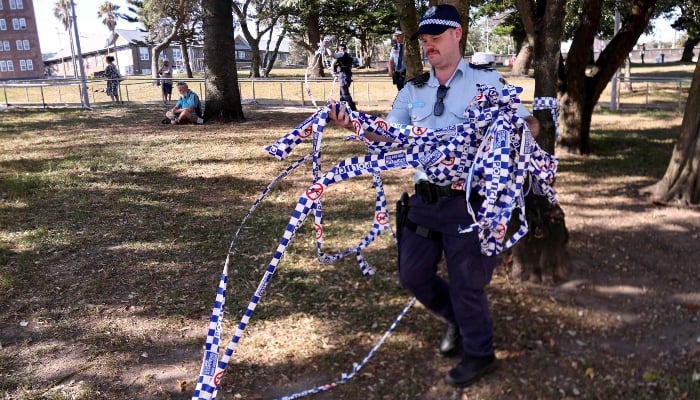 Police officers remove police tape from the scene of Sundays shooting at Bondi Beach, in Sydney on December 17, 2025. — AFP