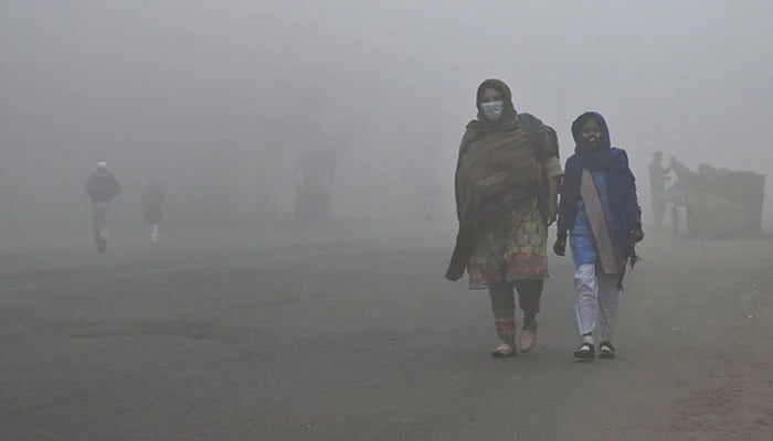 A student walks with her mother to school amid foggy weather in Lahore, on December 21, 2022. — AFP