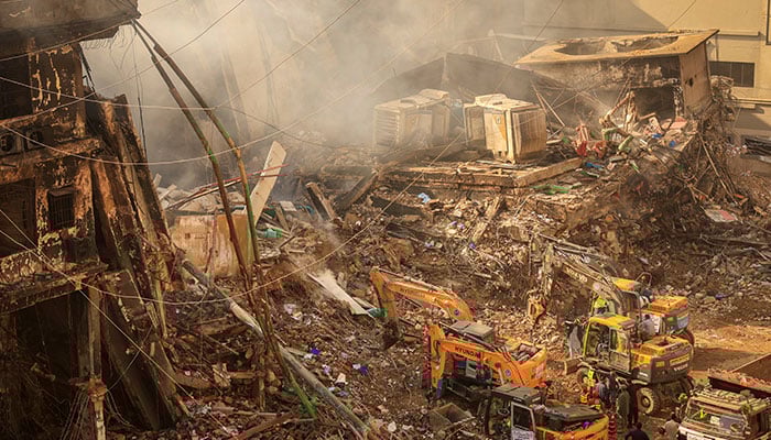 Emergency personnel stand as heavy machinery clears the site following a massive fire that broke out in the Gul Plaza Shopping Mall in Karachi on January 20, 2026. — Reuters