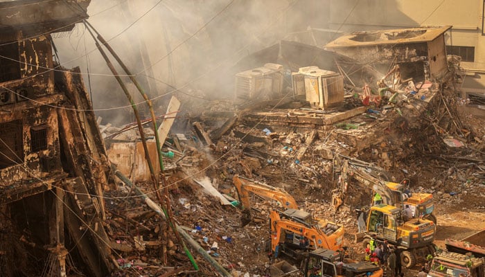 Emergency personnel stand as heavy machinery clears the site following a massive fire that broke out in the Gul Plaza Shopping Mall in Karachi, January 20, 2026. — Reuters