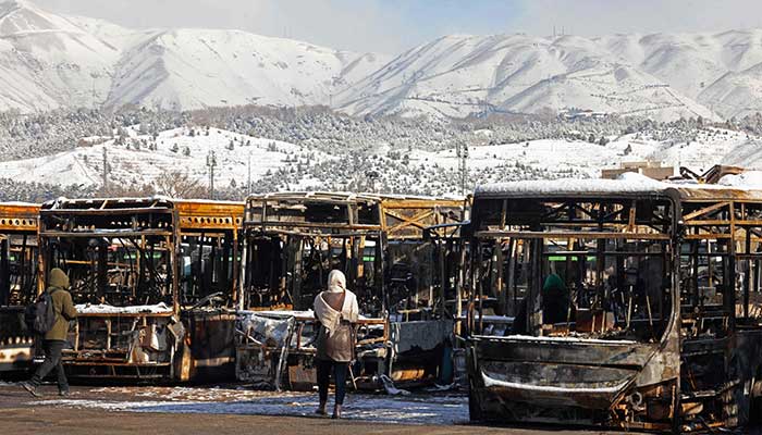 This photograph taken during a tour for foreign media shows media representatives walking past the parked buses that were burnt at a depot during recent public protests, in Tehran on January 21, 2026. — AFP