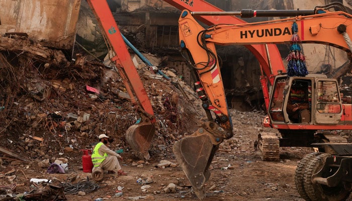 A worker takes a break next to heavy machinery used to clear the site, following a massive fire that broke out in the Gul Plaza Shopping Mall in Karachi, January 22, 2026. — Reuters