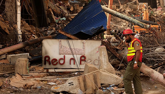 A rescue worker walks past a signboard of a damaged shop, following a massive fire that broke out in the Gul Plaza shopping centre in Karachi on January 22, 2026. — Reuters