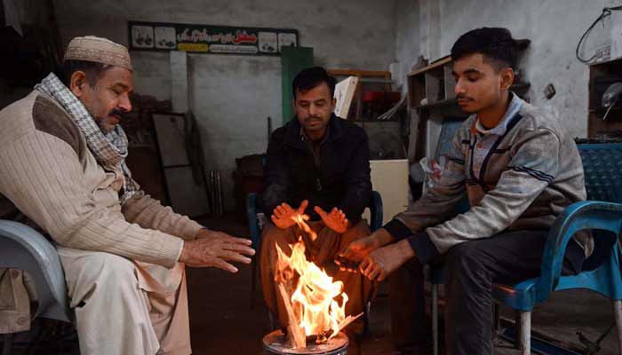 People are sitting around fire to keep themselves warm during cold weather in the Federal Capital.— APP