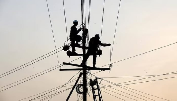 Technicians are silhouetted as they fix cables on a power transmission line in Karachi, Pakistan, January 9, 2017. — Reuters