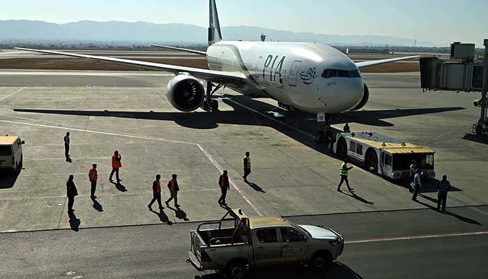 Ground staff stand next to the Pakistan International Airlines (PIA) aircraft ahead of its takeoff for Paris at the Islamabad International Airport on January 10, 2025. — INP
