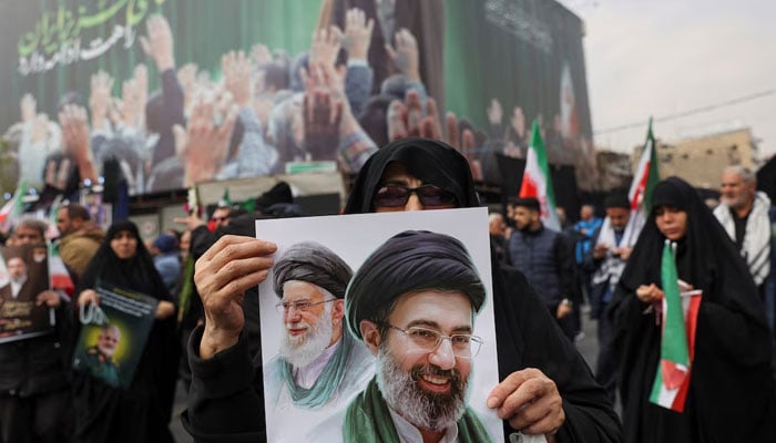 A woman holds an image of Irans new supreme leader, Mojtaba Khamenei, alongside late Iranian Supreme Leader Ayatollah Ali Khamenei, during a funeral ceremony for the Iranian military commanders who were killed in strikes, amid the US-Israeli conflict with Iran, in Tehran, Iran, March 11, 2026. — Reuters