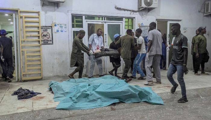 People carry an injured man past bodies covered with sheets at a hospital in Maiduguri on March 16, 2026, following blasts in the city. — AFP
