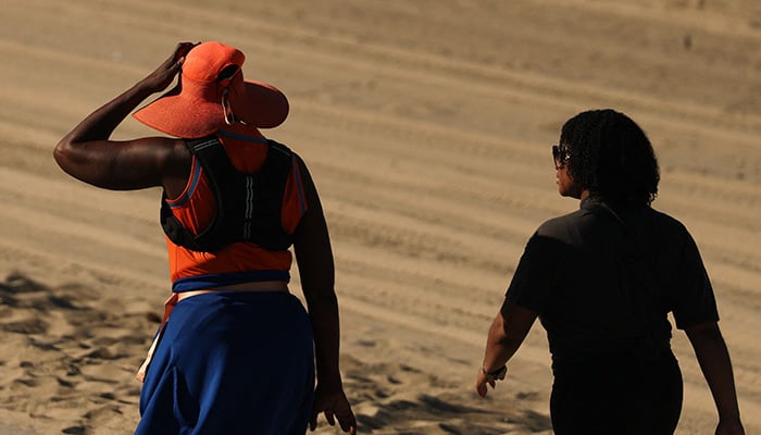 A person wears a hat for shade under the morning sun while walking along The Strand in Redondo Beach, California on March 20, 2026, during a heat wave. — AFP