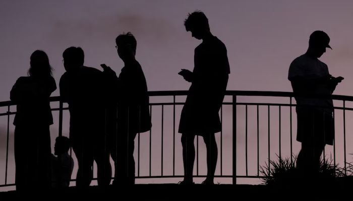 People use their mobile phones at dusk in Brisbane, Australia, December 8, 2025. — Reuters