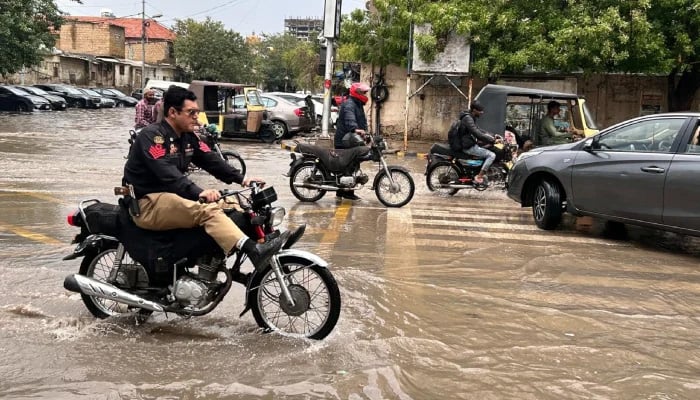 A policeman tries to evade water while riding his bike through flooded road after heavy rainfall in Karachi on April 2, 2026. — Geo.tv