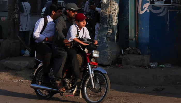Students ride on a motorbike while heading to school in Karachi, March 10, 2026. — Reuters
