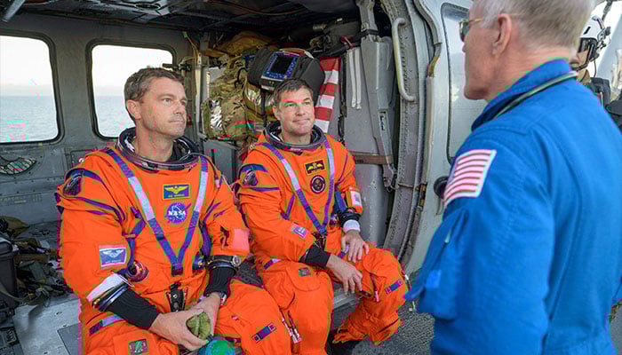 This handout photo released by Nsaa shows Nasa astronaut Reid Wiseman, Artemis II commander, (L) and CSA (Canadian Space Agency) astronaut Jeremy Hansen, Artemis II mission specialist, talking with Nasa Flight Surgeon Richard Scheuring at their Navy MH-60 Seahawk from Helicopter Sea Combat Squadron (HSC) 23 on the flight deck of USS John P Murtha after they and fellow crewmates were extracted from their Orion spacecraft after splashdown, April 10, 2026, in the Pacific Ocean off the coast of California. — AFP