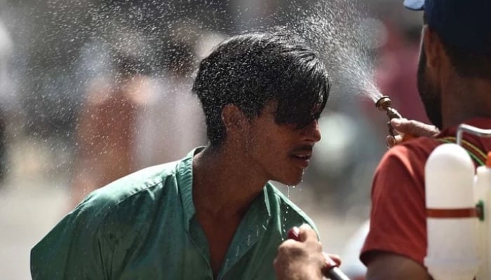 An Edhi volunteer sprays water on a person along a street during a hot summer day in Karachi. — INP/File