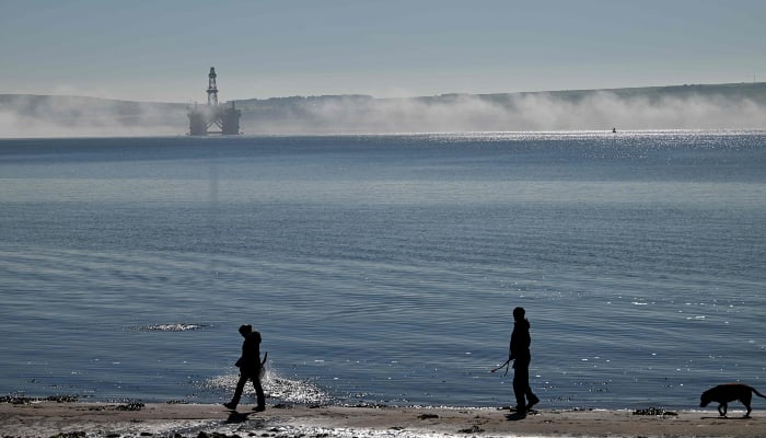 A dog is walked beside the water as an oil rig is seen through the mist, on the Cromarty Firth on the north-east coast of Scotland on April 24, 2026. — AFP