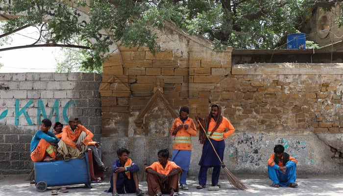 A group of Sindh Solid Waste Management Board (SSWMB) workers with dustbins and brooms, take shelter under a tree as they take a break while cleaning the roads, in hot and humid weather, in Karachi on May 3, 2026. — Reuters