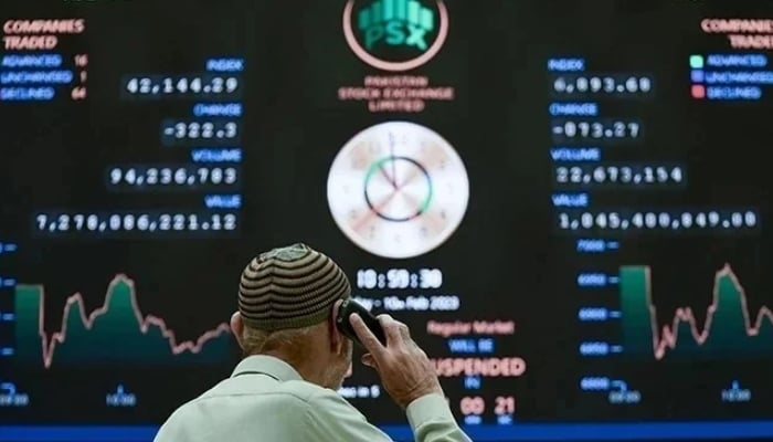 A broker talks on phone as he looks at an index board showing the latest share prices at the PSX in Karachi. — AFP/File