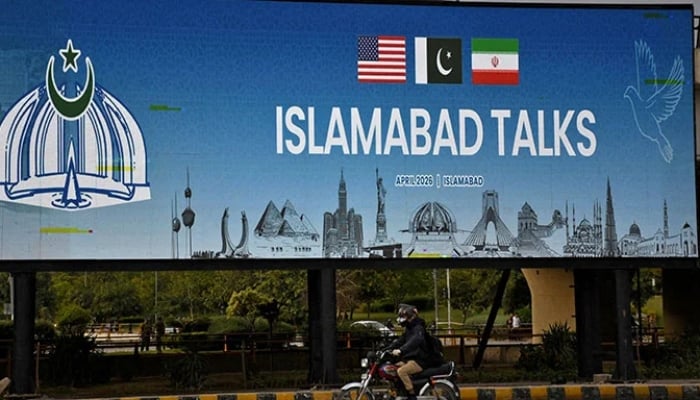 A man rides his motorbike past a billboard installed alongside a road ahead of the US-Iran peace talks, in Islamabad, April 10, 2026. — Reuters