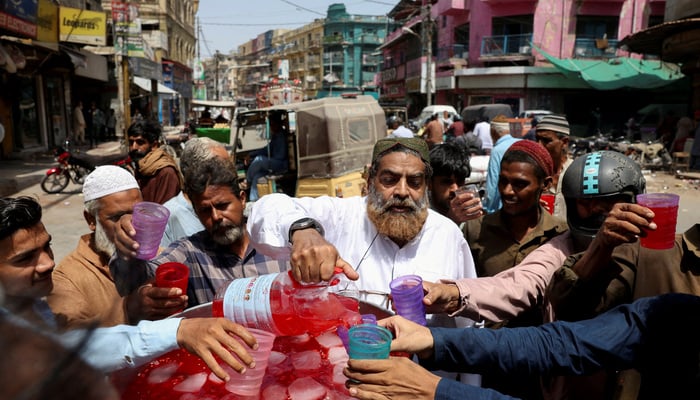 People receive free chilled rose-flavored syrup beverage to cool off during a hot summer day, along Burnes Road, a food street located in Karachi on May 7, 2026. — Reuters