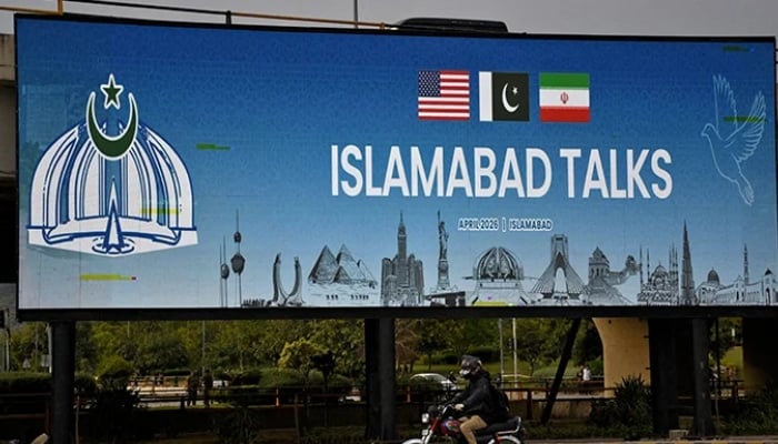 A man rides his motorbike past a billboard installed alongside a road as Pakistan prepares to host the US and Iran for peace talks, Islamabad, April 10, 2026. — Reuters