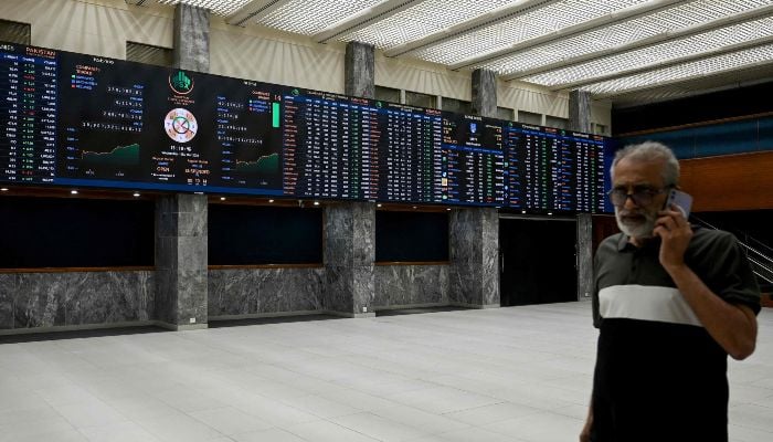 A stock broker walks past a digital board showing share prices at the Pakistan Stock Exchange (PSX) in Karachi on March 25, 2026. — AFP