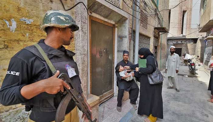 A policeman stands guard as a health worker administers polio drops to a child during a polio vaccination campaign in Peshawar. — AFP/File