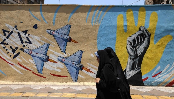 Iranian women walk past an anti-US and anti-Israeli mural in Tehran on June 3,2026. — AFP