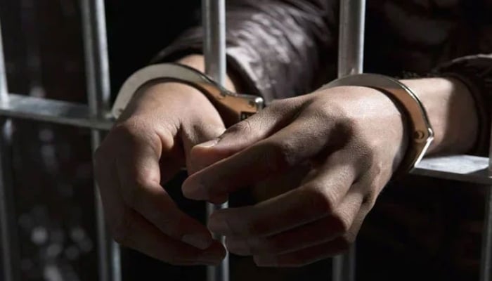 A representational image of a handcuffed man standing behind bars. — APP/File
