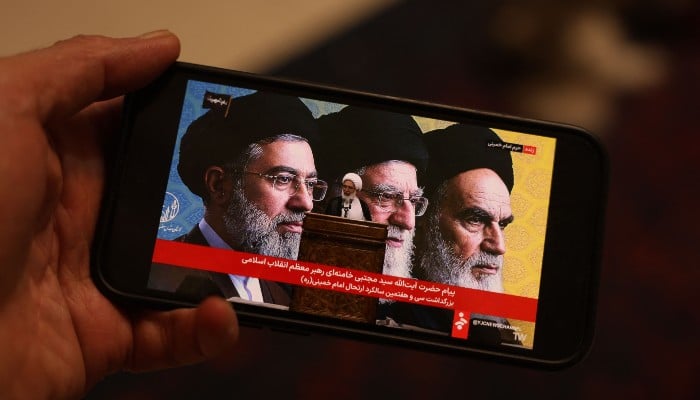 This illustration photograph taken on June 4, 2026, shows a man watching the live streaming on his mobile phone of an Iranian official reading a message by Irans supreme leader Ayatollah Mojataba Khamenei to the public at the tomb of the countrys late supreme leader Ayatollah Ruhollah Khomeini, in Tehran on June 4, 2026. — AFP