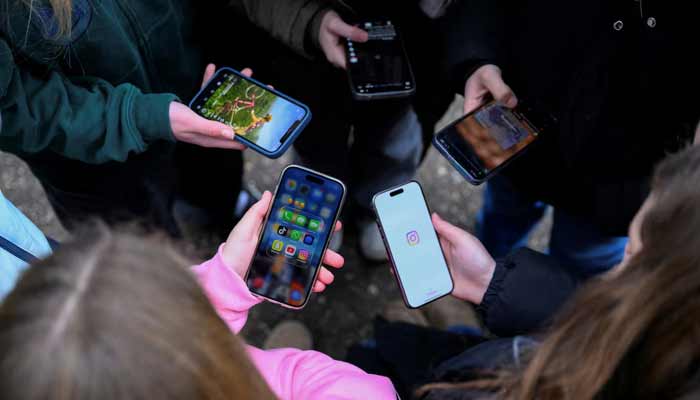 Teenagers pose for a picture while looking at their phones, in Bonn, Germany, February 20, 2026.— Reuters/File