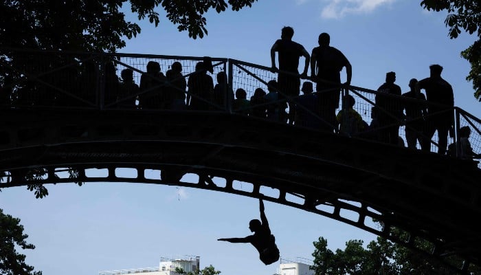 Young people jump from a bridge into the Canal Saint-Martin during a heatwave in Paris on June 22, 2026. — AFP