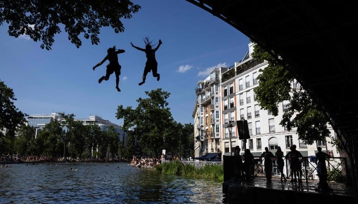 Young people jump from a bridge into the Canal Saint-Martin during a heatwave in Paris on June 22, 2026. — AFP