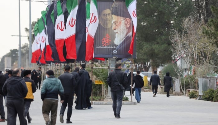 People walk along a street with Iranian flags and a poster with images of Irans late Supreme Leader Ayatollah Ali Khamenei, amid the US-Israeli conflict with Iran, in Tehran, Iran, March 9, 2026. — Reuters